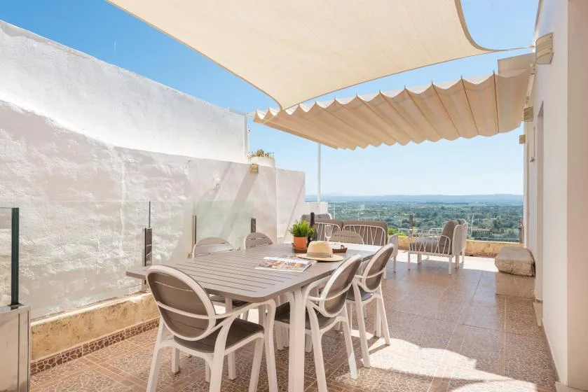 An outdoor dining area with a table and seating beneath a fabric shade.