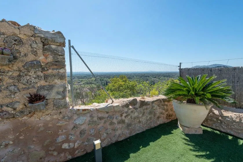 An outdoor terrace with a stone wall, potted plants, and a distant landscape view.