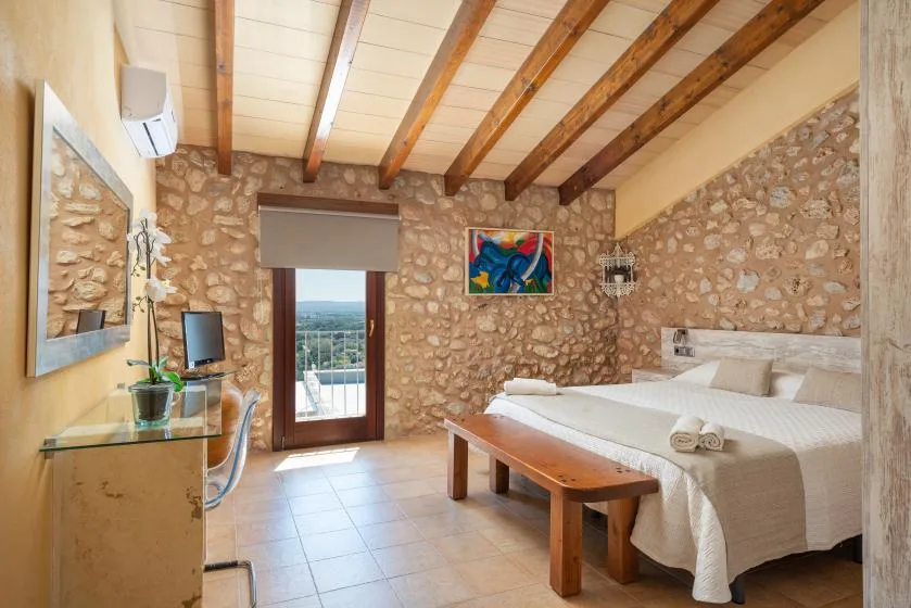 A bedroom with a double bed, exposed wooden ceiling beams, and stone walls.