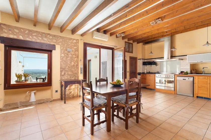 An open-plan kitchen and dining area with a wooden table beneath exposed ceiling beams.