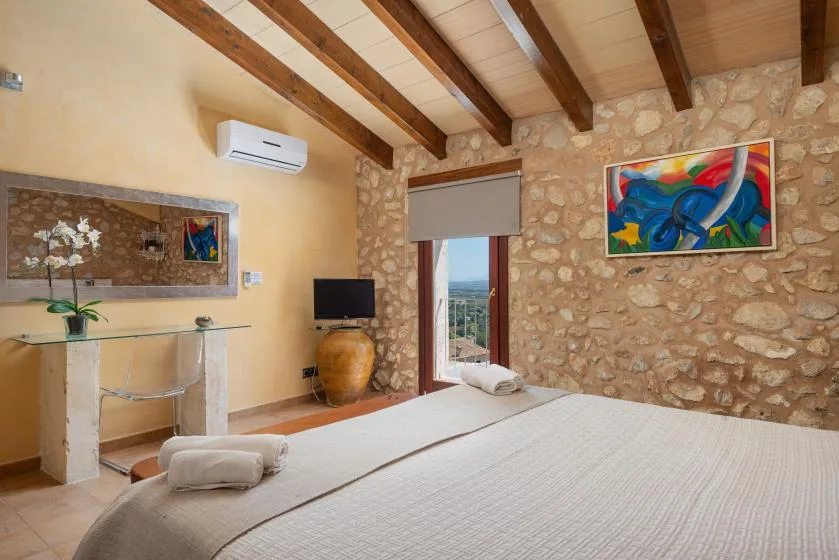 A bedroom with a bed, stone walls, and a doorway opening to a balcony.