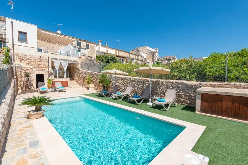 An outdoor swimming pool is surrounded by lounge seating, umbrellas, and stone walls.