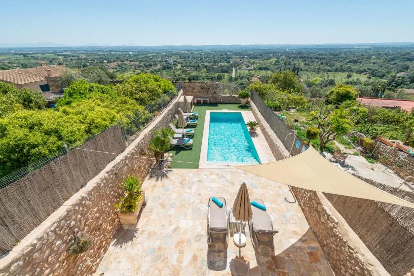 An outdoor swimming pool sits beside a stone-paved terrace overlooking green countryside.