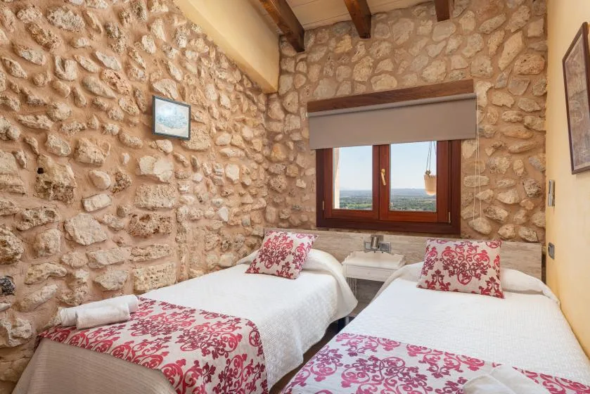 A stone-walled bedroom with two single beds beneath a window.