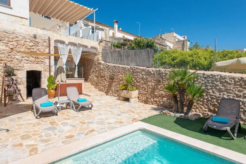 A sunny stone patio beside a small swimming pool and outdoor seating.