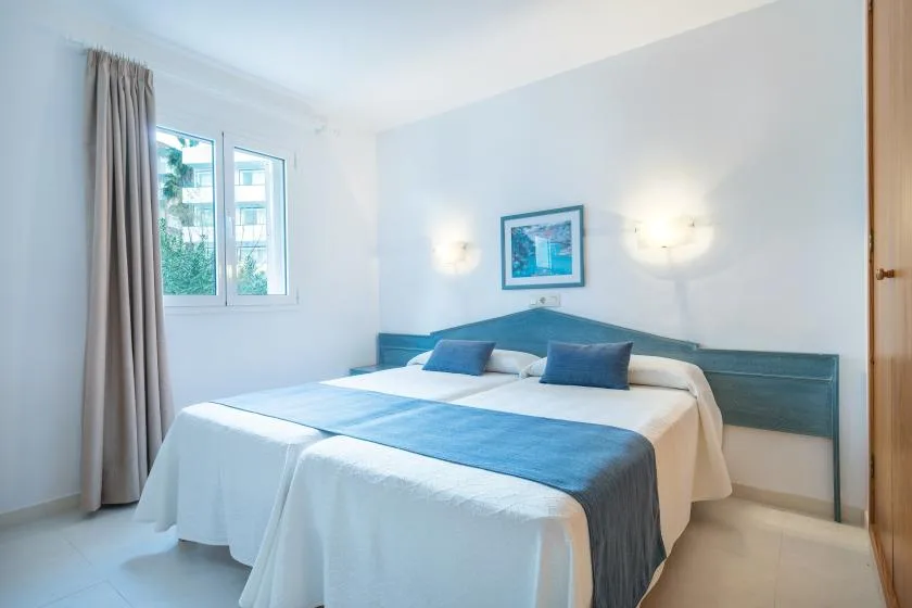 A bright bedroom with a neatly made bed beneath a framed picture.