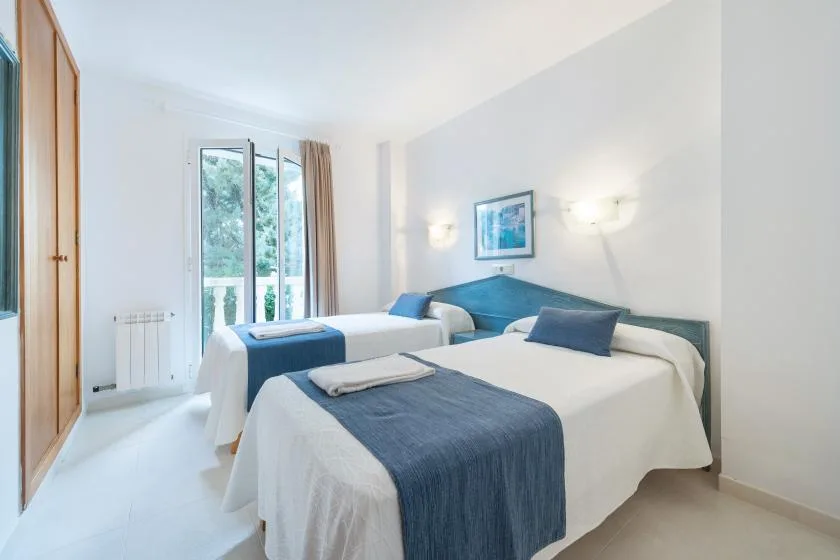 A bright bedroom with two beds dressed in white and blue linens.