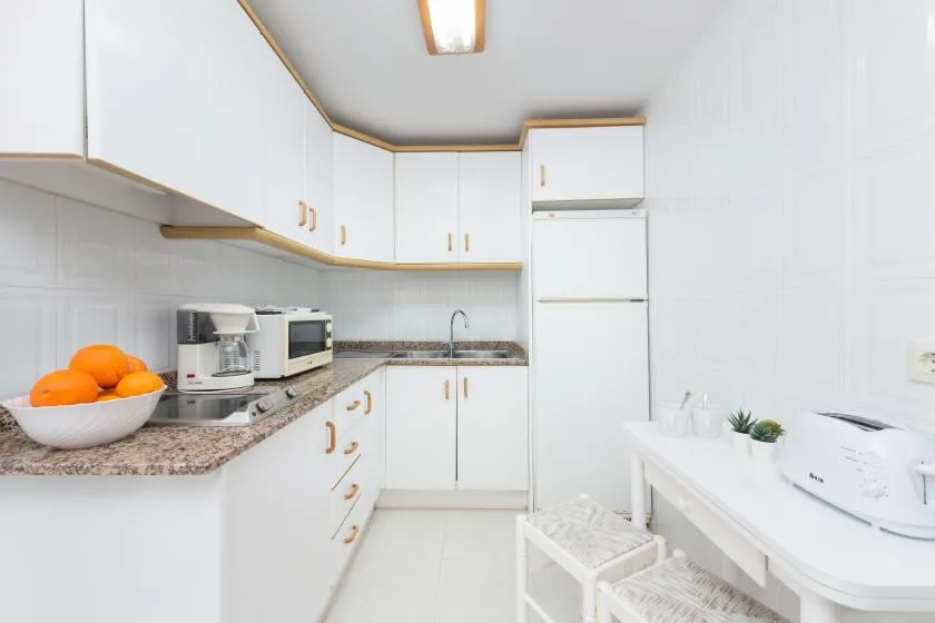 A bright kitchen with white cabinets, a refrigerator, and a long counter.