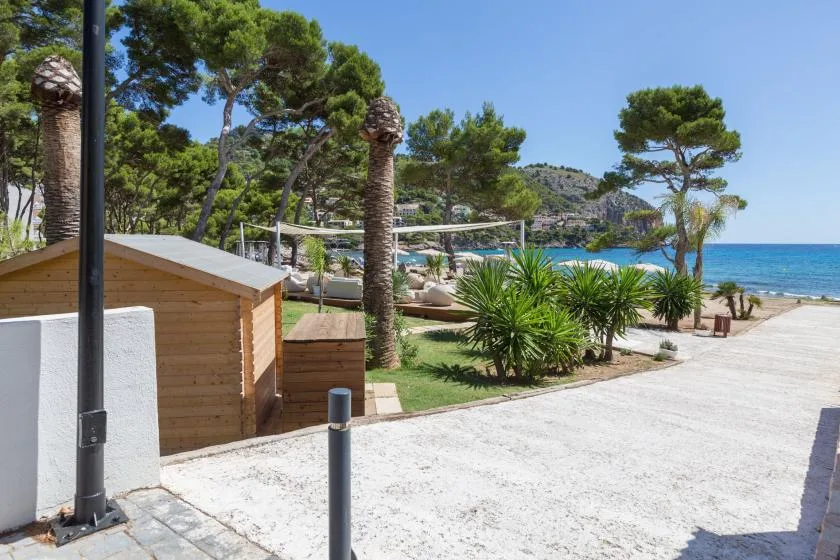 A landscaped seaside path with trees, greenery, and the blue sea beyond.