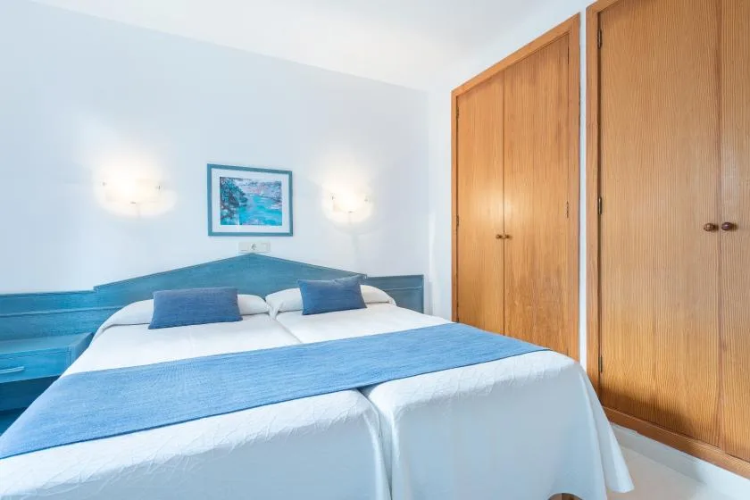 A bedroom with white bedding, blue accents, and wooden wardrobes.