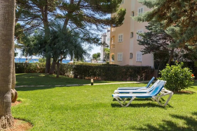 A grassy garden with two lounge chairs beneath trees beside a building.