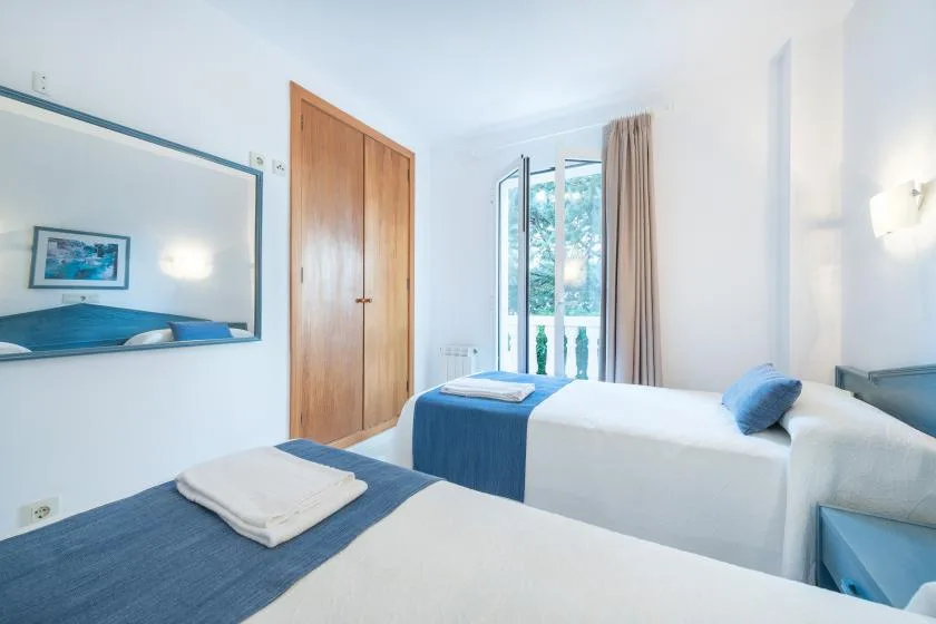 A bright bedroom with white bedding, blue accents, and a window.