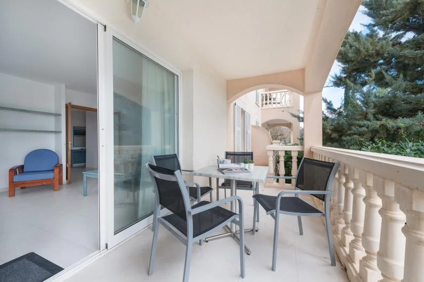 A covered balcony with a table and seating overlooks trees and neighboring buildings.