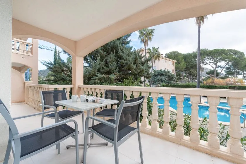 Covered outdoor terrace with seating overlooking a swimming pool and leafy surroundings.