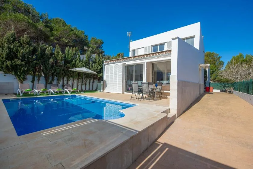 Una casa moderna da a una piscina azul y una terraza con asientos.