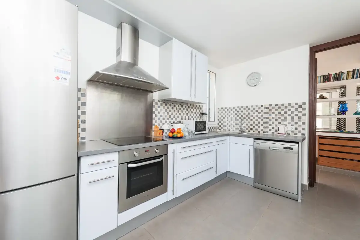 Una cocina luminosa con armarios blancos, electrodomésticos de acero inoxidable y salpicadero de azulejos.