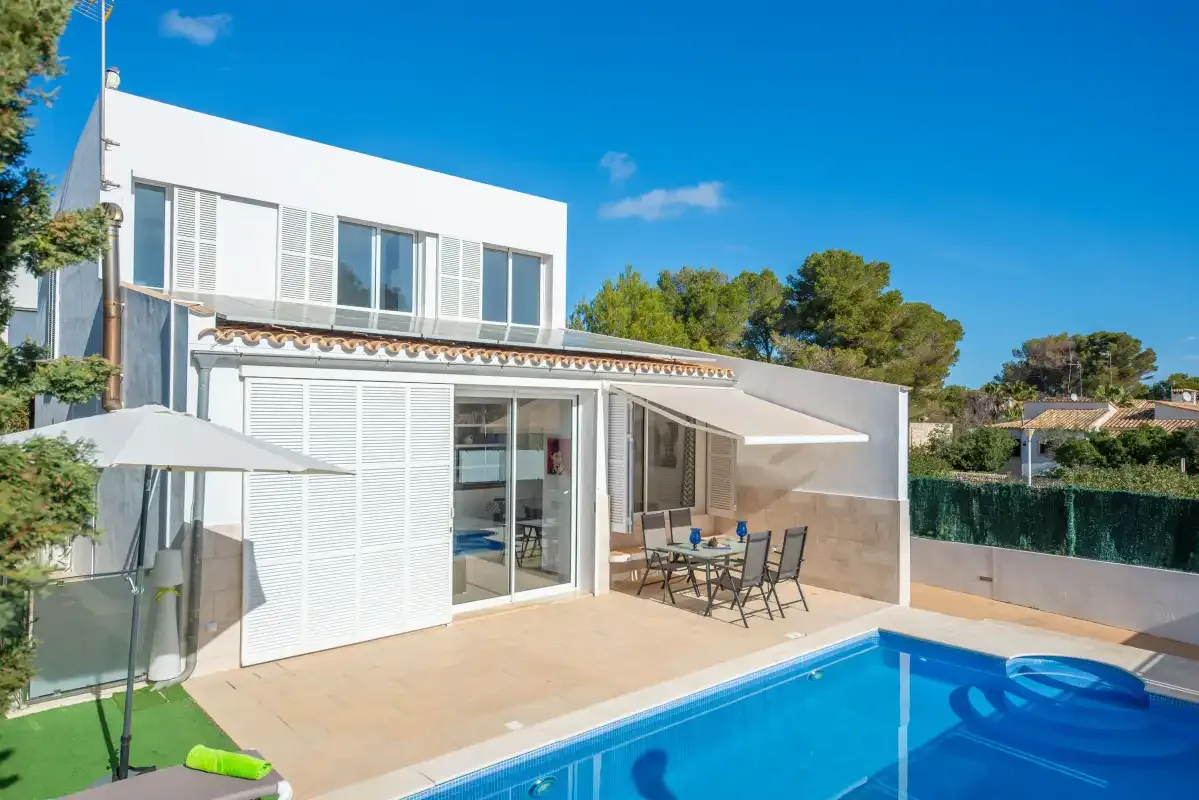 Una casa blanca moderna se abre a un patio junto a una piscina.