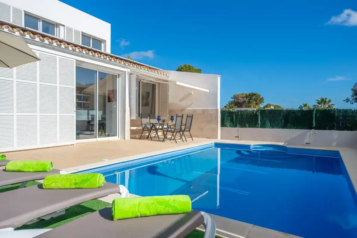 Una piscina junto a una casa moderna, con asientos al aire libre en la terraza.