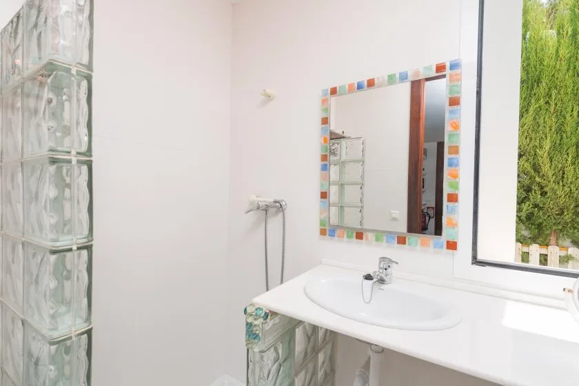 Un lavabo de baño con espejo de marco colorido junto a una pared de bloques de vidrio.