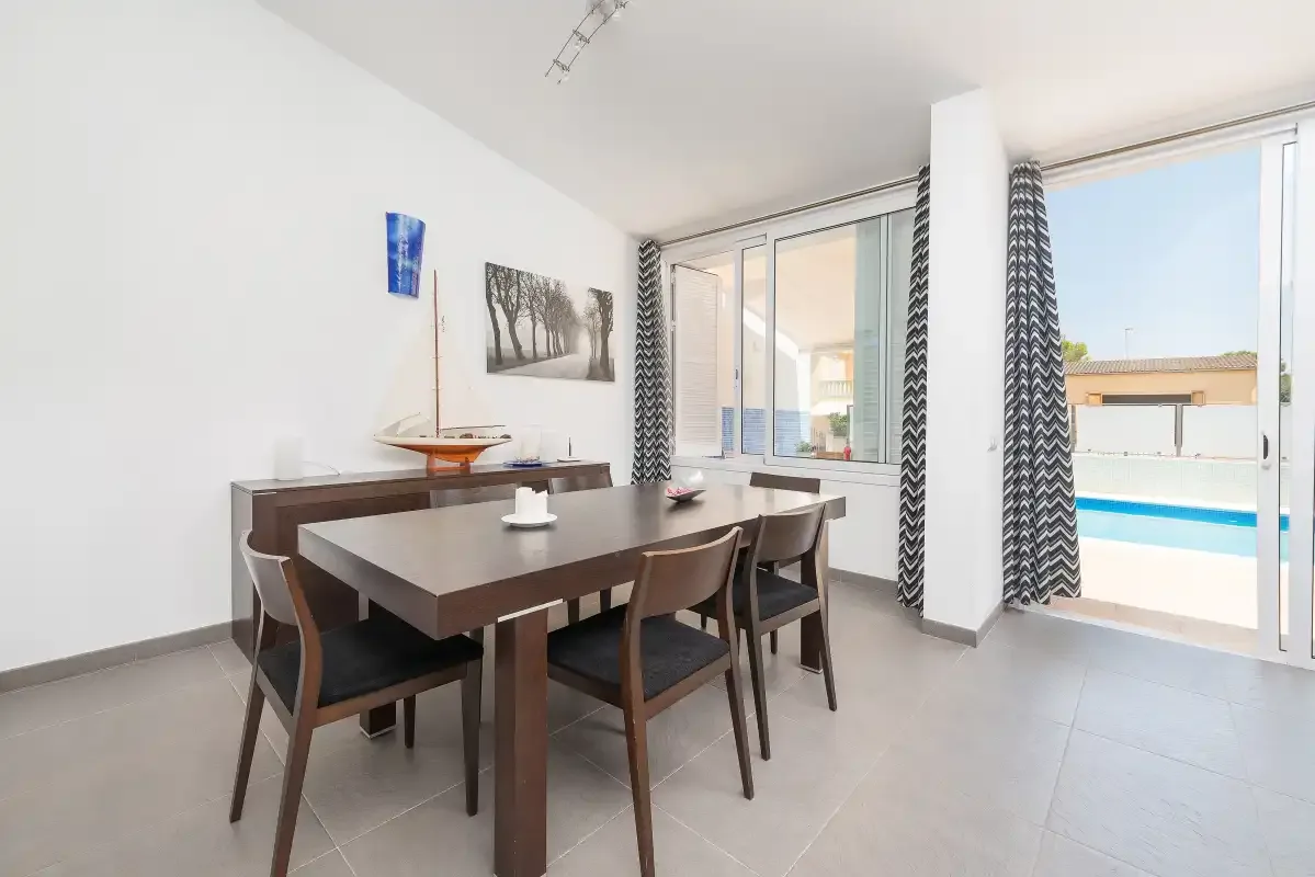 Comedor con mesa y asientos junto a ventanas con vistas a una piscina.