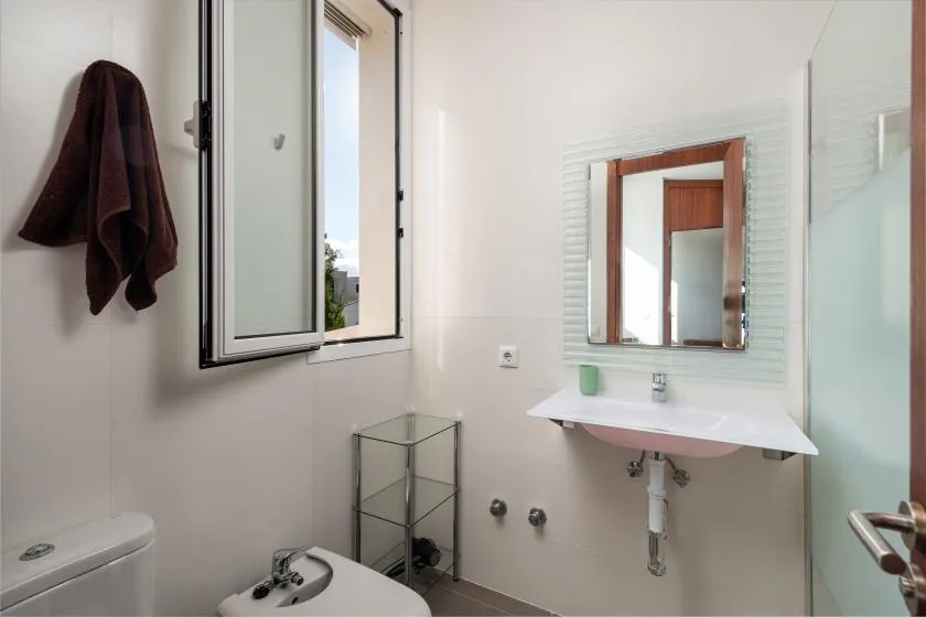 Un baño luminoso con un lavabo suspendido y una ventana abierta.