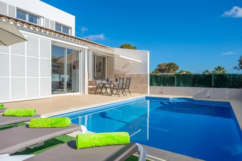 Una piscina junto a una casa moderna, con asientos al aire libre en el patio.
