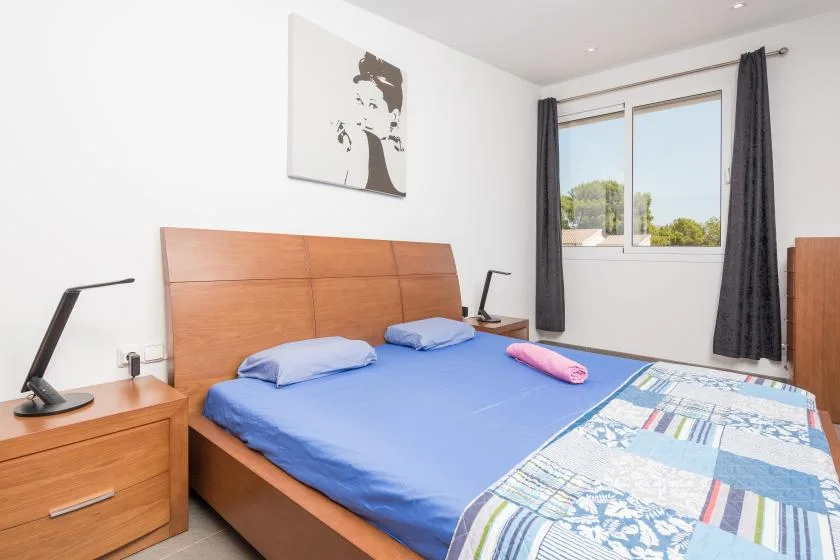 Un dormitorio luminoso con una cama grande, ropa de cama azul y una ventana con cortinas oscuras.