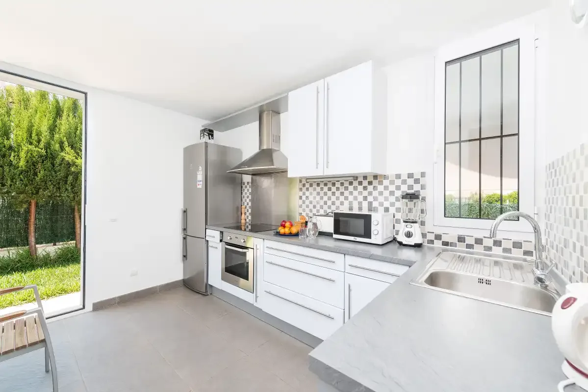 Una cocina luminosa con armarios blancos, electrodomésticos de acero inoxidable y vistas al jardín.