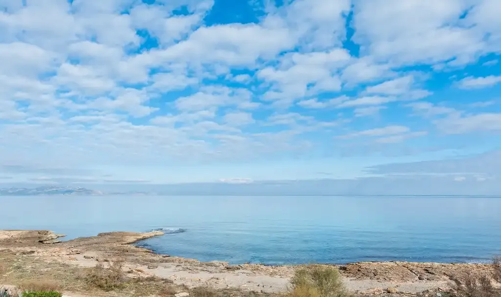 Un paisaje marino con costa rocosa bajo un cielo parcialmente nublado.