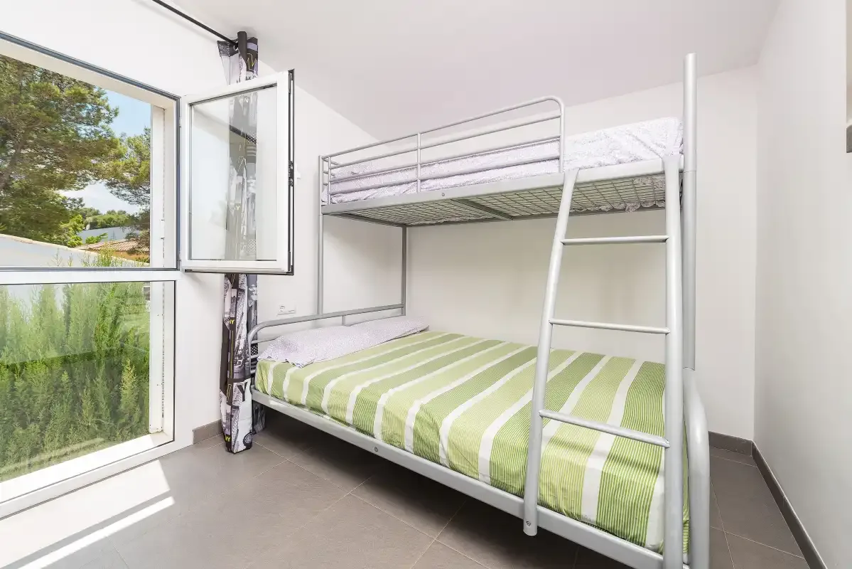Un dormitorio con una litera de rayas verdes junto a una ventana abierta.