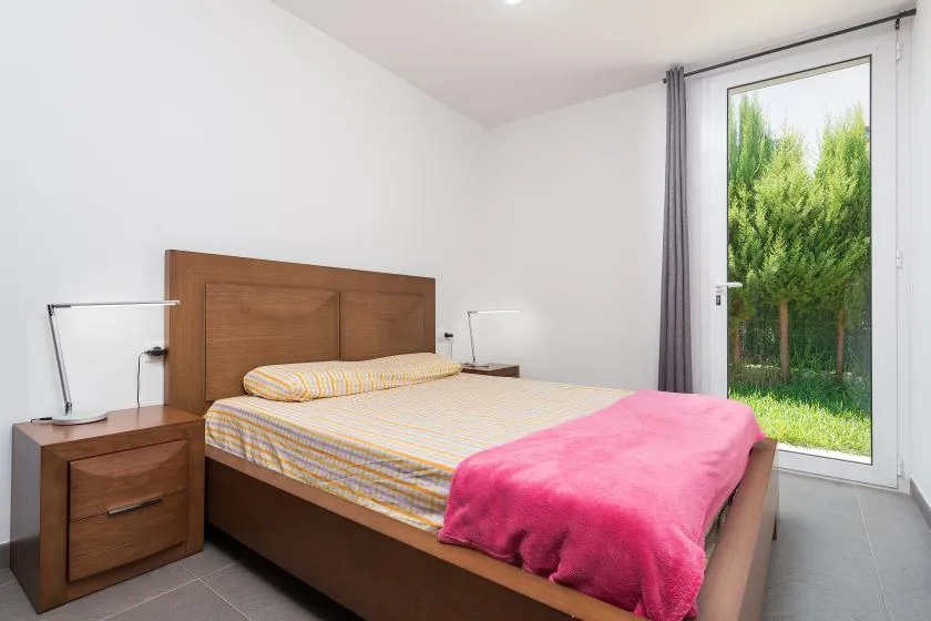 Un dormitorio con una cama de madera, ropa de cama colorida y una puerta de vidrio con vista a la vegetación.