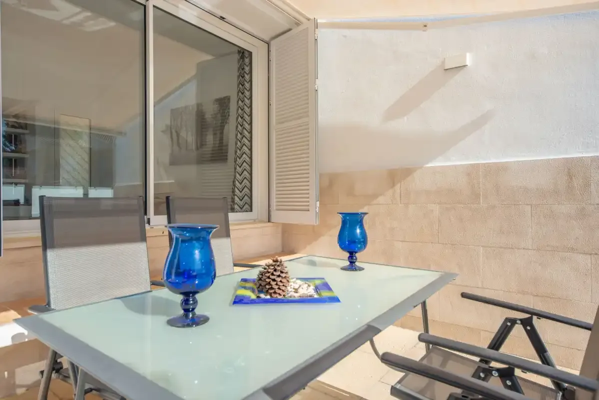 Una zona de comedor en el patio con una mesa de cristal y jarrones decorativos azules.