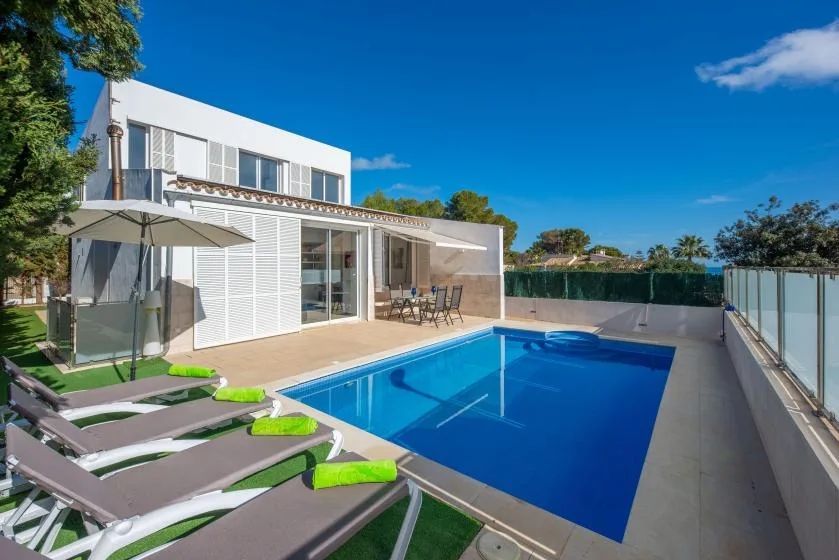 Una casa moderna da a una piscina, con tumbonas en el patio.