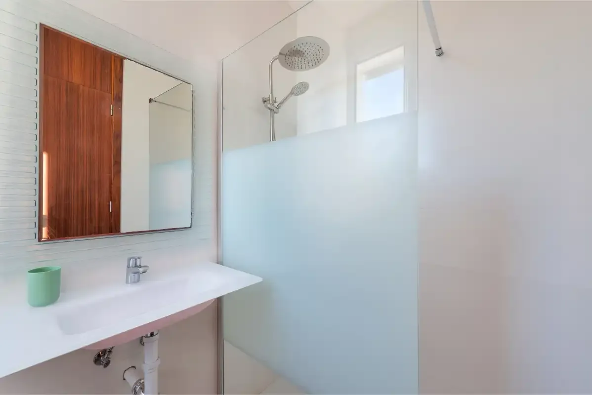 Baño con lavabo y ducha detrás de un panel de vidrio esmerilado.