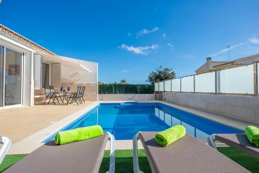 Una piscina al aire libre junto a un patio soleado con tumbonas.