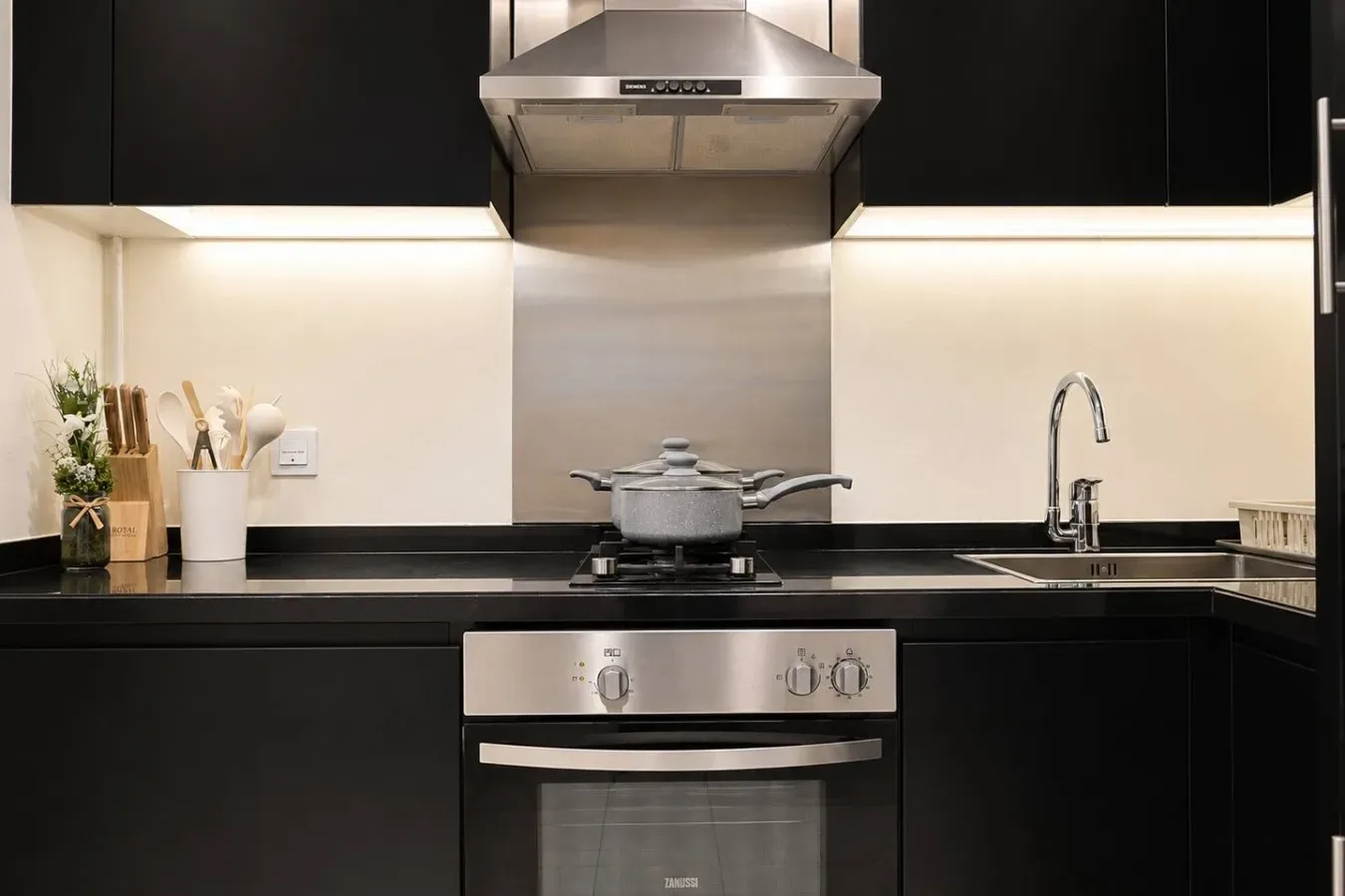 Una cocina moderna con estufa, horno y fregadero bajo gabinetes oscuros.