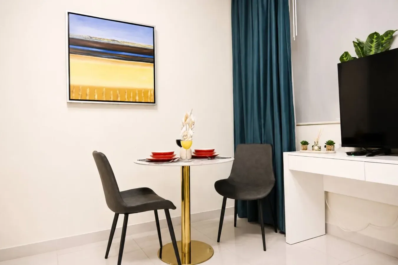 Un pequeño comedor con una mesa redonda y dos sillas junto a cortinas verde azulado.