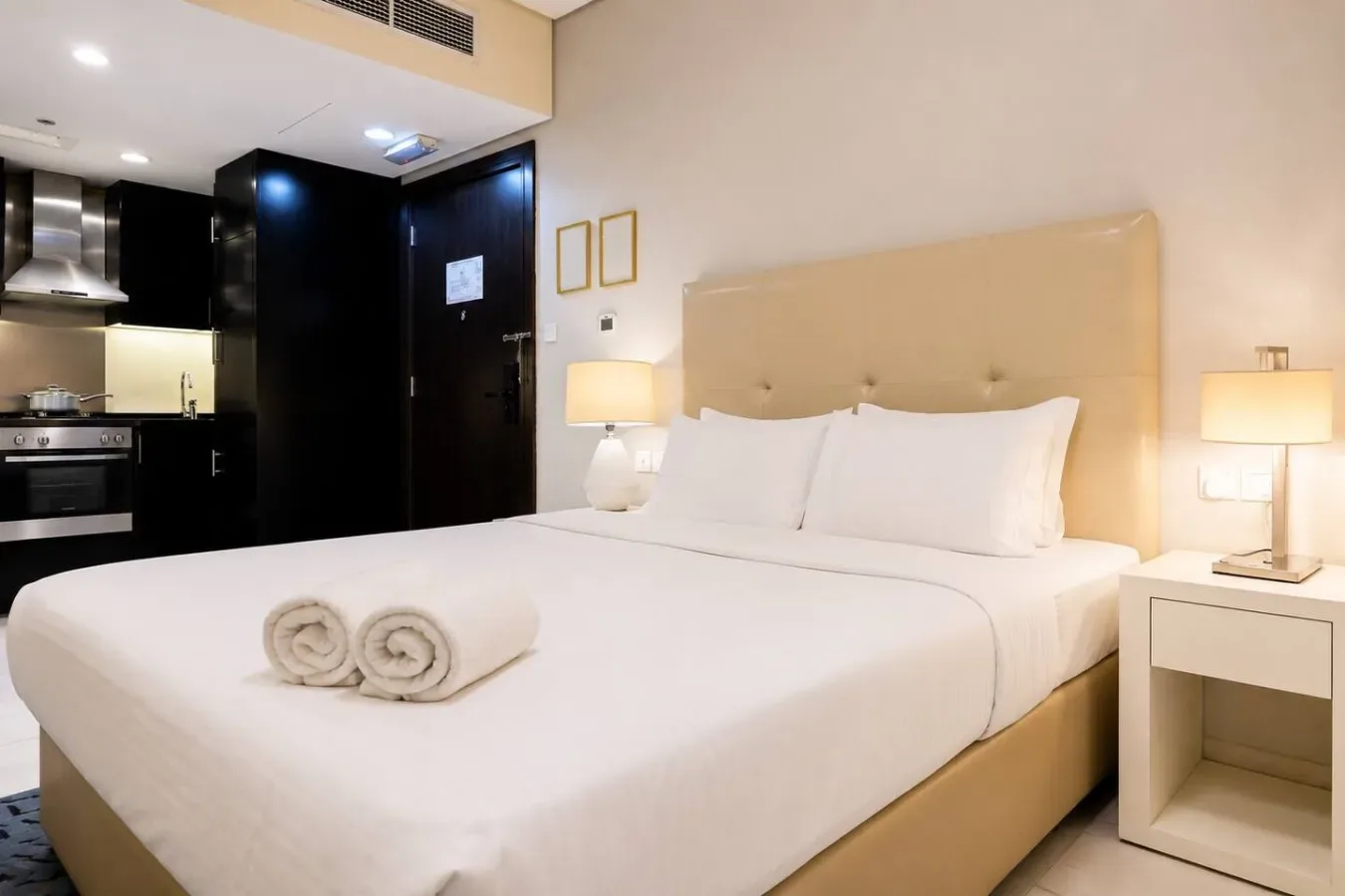 A bedroom with a neatly made bed and a kitchenette in the background.
