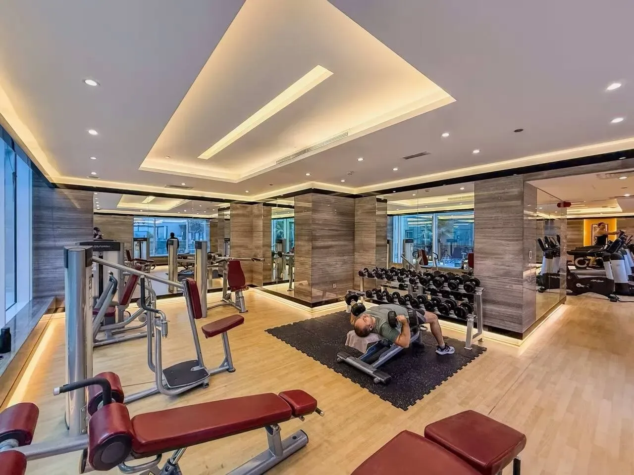 Un gimnasio luminoso con máquinas de ejercicio, pesas y suelo en tonos de madera.