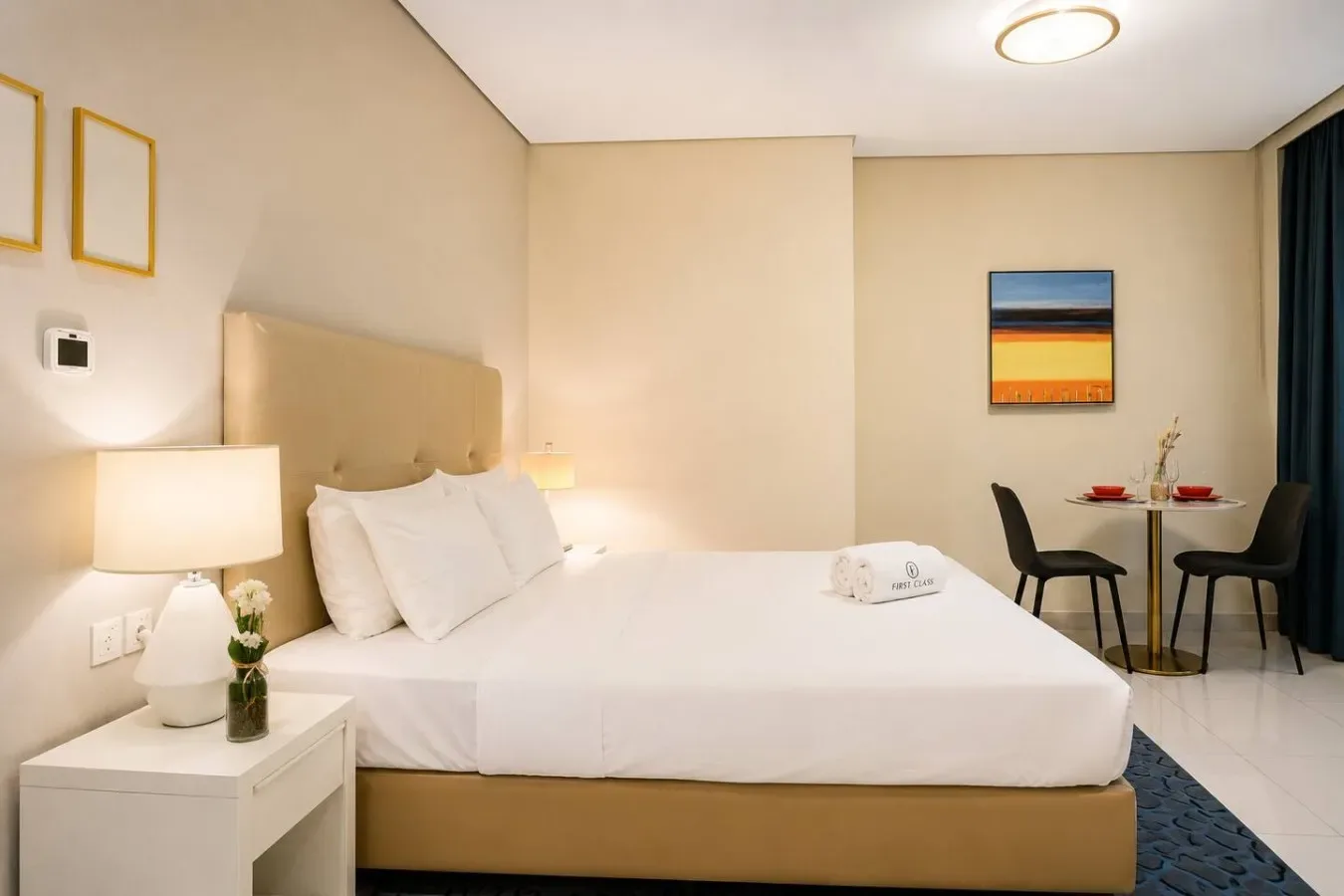 Un dormitorio con una cama bien hecha, lámparas de noche y una mesa pequeña con sillas.