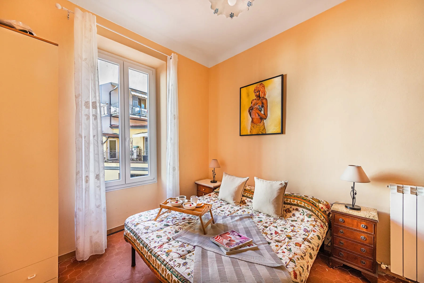 A bedroom with a patterned bed, bedside table, and large window.