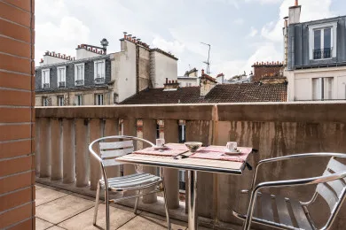 A small outdoor terrace has a table and seating overlooking nearby rooftops.