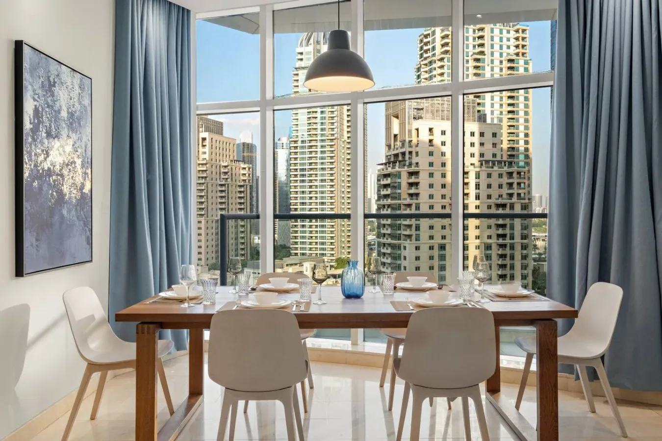 Un comedor con una mesa larga junto a grandes ventanales con vistas a edificios de la ciudad.