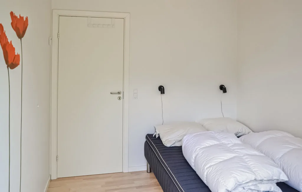 Un dormitorio con una cama tendida y sencillas luces montadas en la pared.