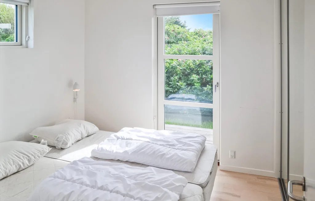 Un dormitorio luminoso con dos camas bajo una ventana alta.