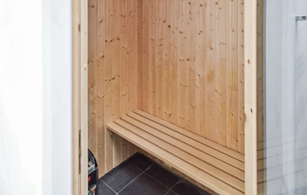 Una sauna revestida de madera con un banco largo y suelo de baldosas oscuras.