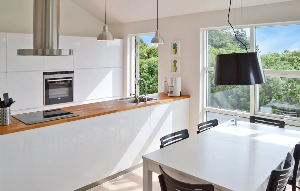 Una cocina moderna y luminosa con comedor, una encimera larga y grandes ventanas.
