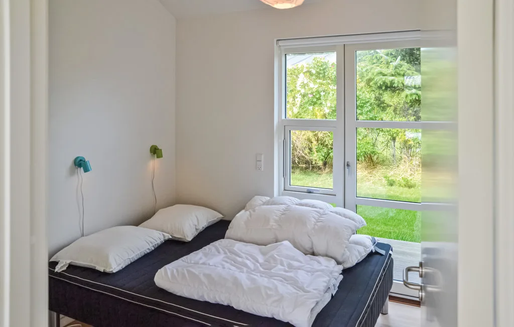 Un dormitorio con una cama, ropa de cama blanca y una ventana grande.