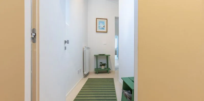 A bright hallway with a striped rug and a small green table.