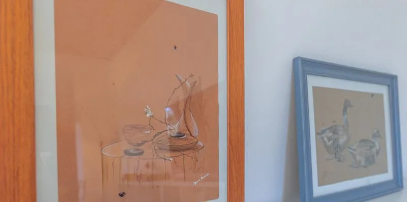 Two framed artworks hang on a pale wall.